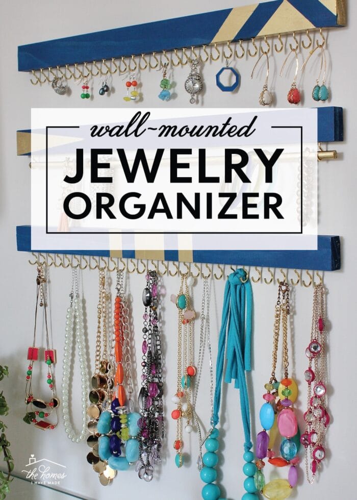 Blue and gold painted boards with brass cup hooks holding colorful necklaces and earrings, under a jewelry organizer title