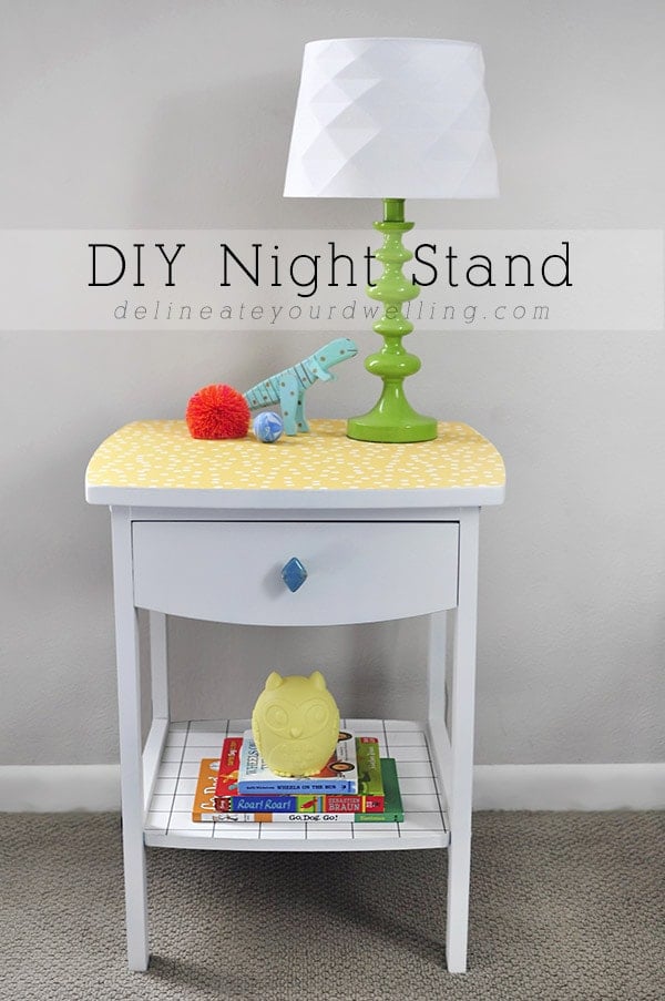 White nightstand with a yellow patterned wallpaper top, a blue knob drawer and a lower shelf, topped with a green lamp