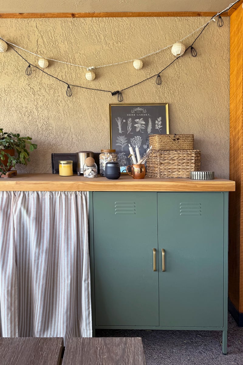 Weatherproof Outdoor Bar Top | DIY Patio Furniture Idea Weatherproof wood outdoor bar top on green metal cabinets under a covered patio with string lights and a botanical print