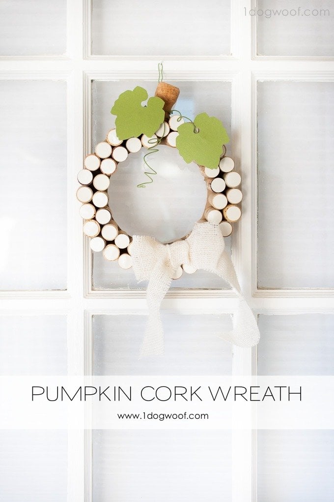 White pumpkin cork wreath of upright corks with a cork stem, green paper leaves and a burlap bow on a white door