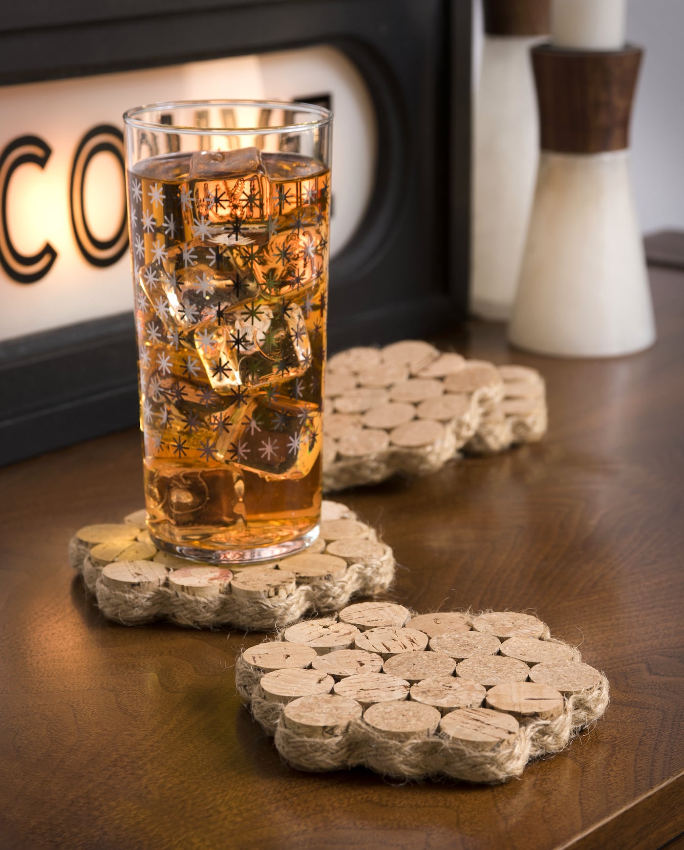 Wine cork coasters made of cork slices edged in twine, one under a glass of iced tea on a wooden side table