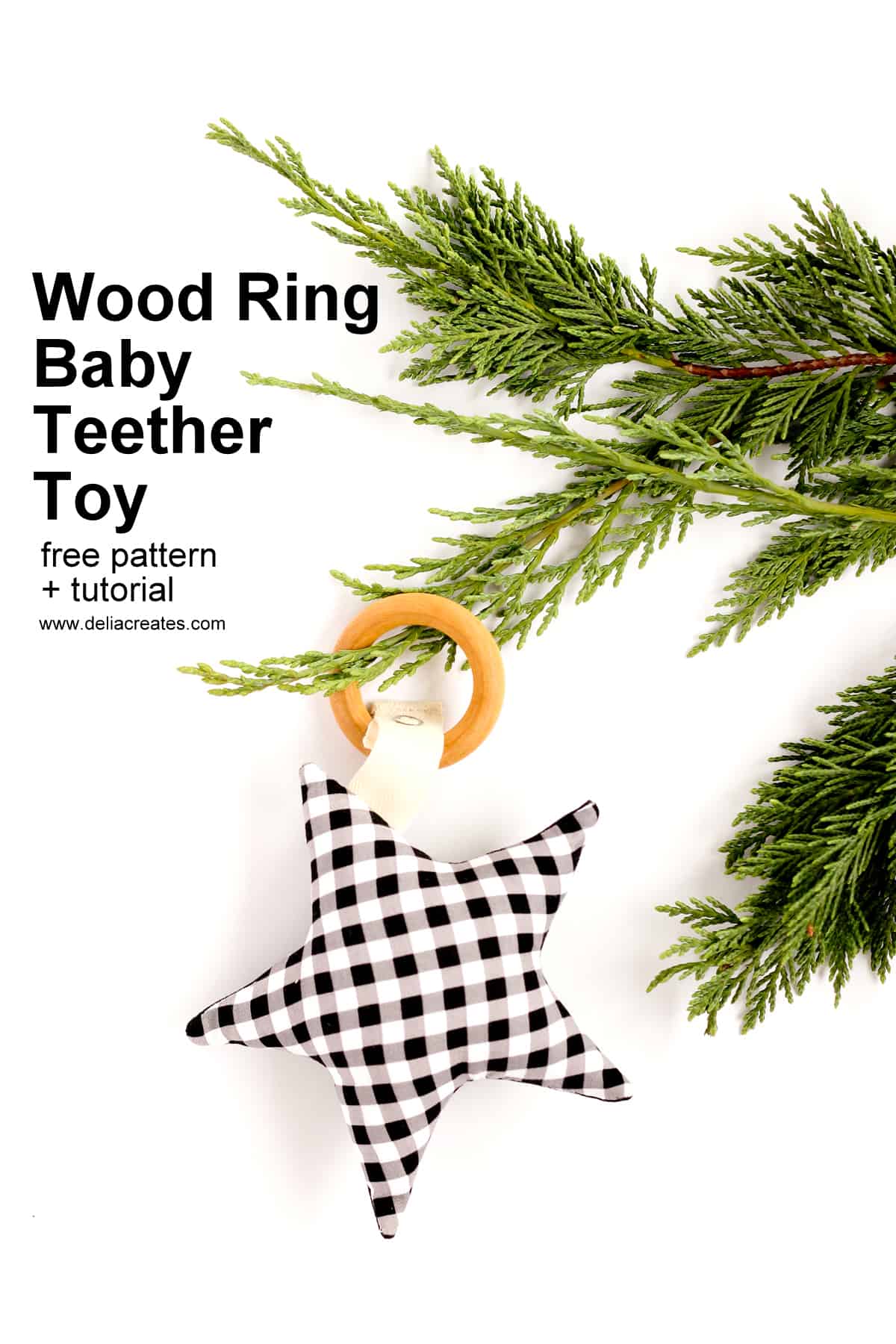 Wooden baby teether ring with a black and white gingham fabric star attached by twill tape beside a sprig of evergreen