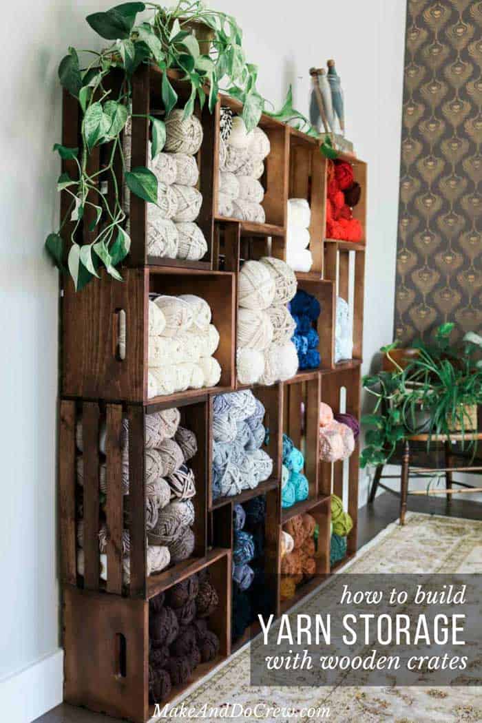 Stacked dark wooden crates forming tall shelves filled with skeins of cream, gray, blue and red yarn beside a trailing plant