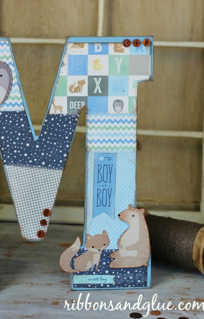 Close view of a letter M covered in blue patchwork baby papers with a fox and bear die cut and red buttons