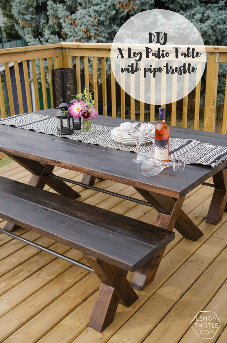 X Leg Patio Table | DIY Patio Furniture Idea Dark stained X leg patio table with a pipe trestle and two matching benches on a wood deck, set with wine and flowers